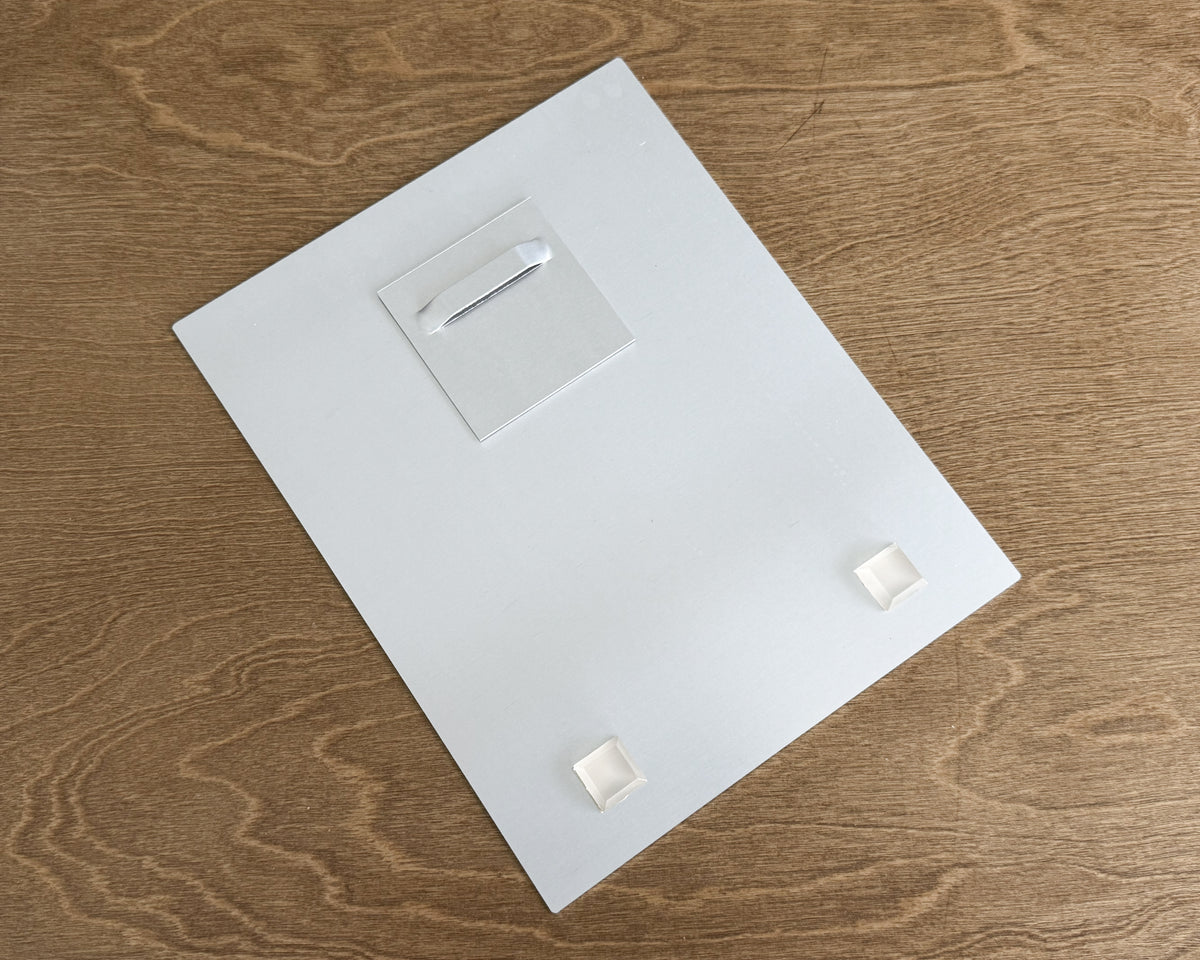 backside of an aluminum hd metal picture frame with a small hanging loop at the top, photographed from above on a brown wood-grain surface.