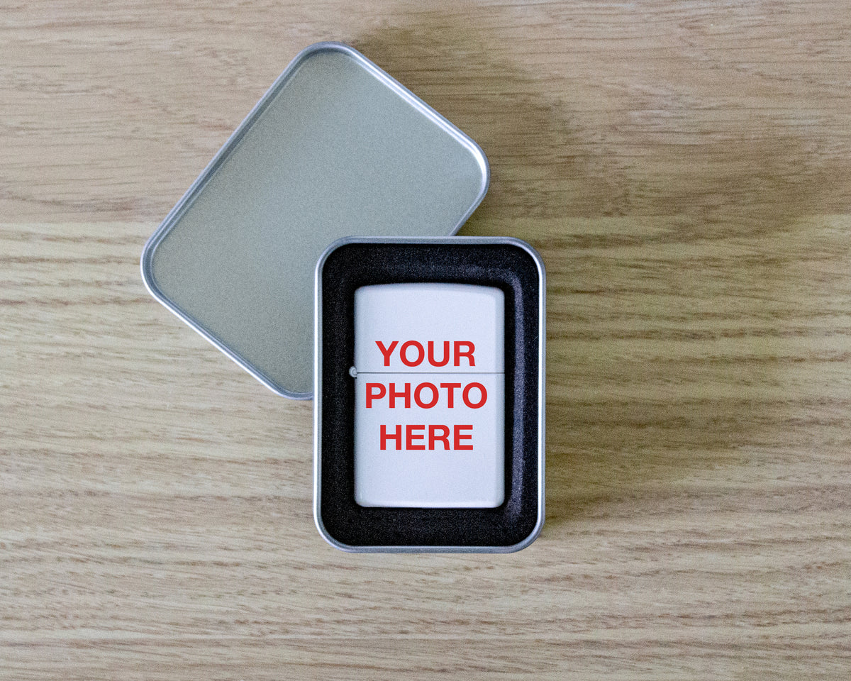 A silver metal tin with its lid off, placed on a light wood surface. The tin contains a white card with red placeholder text reading 'YOUR PHOTO HERE' and a black border around the insert.
