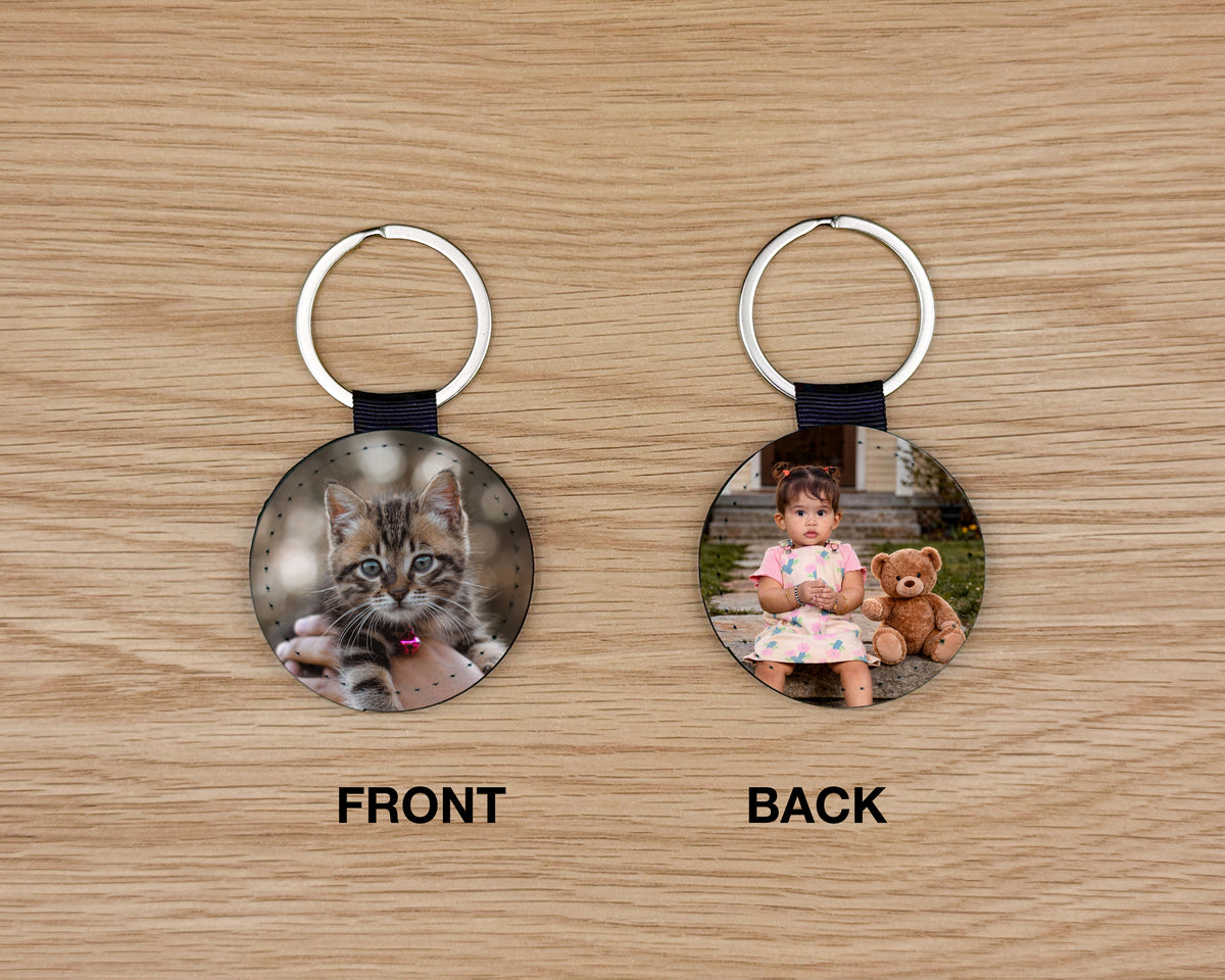 Two circular keychains shown on a wood surface, labeled FRONT and BACK. The front keychain shows a kitten photo with a silver split ring and dark ribbon.