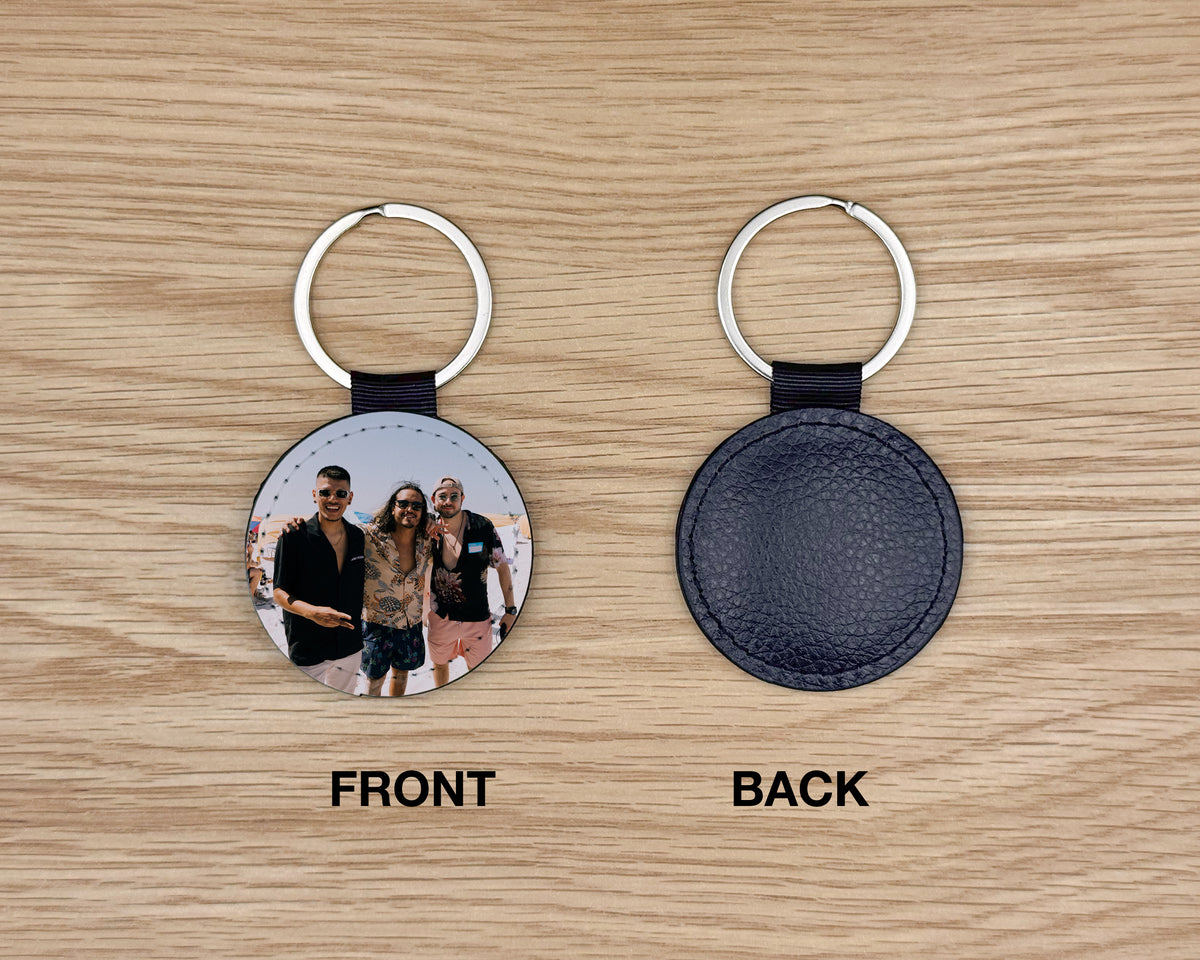 Two views of a round leather keychain on a light wood background: the front shows a printed photo of three people, and the back shows a dark textured leather circle with a silver key ring. Labels below read FRONT and BACK.