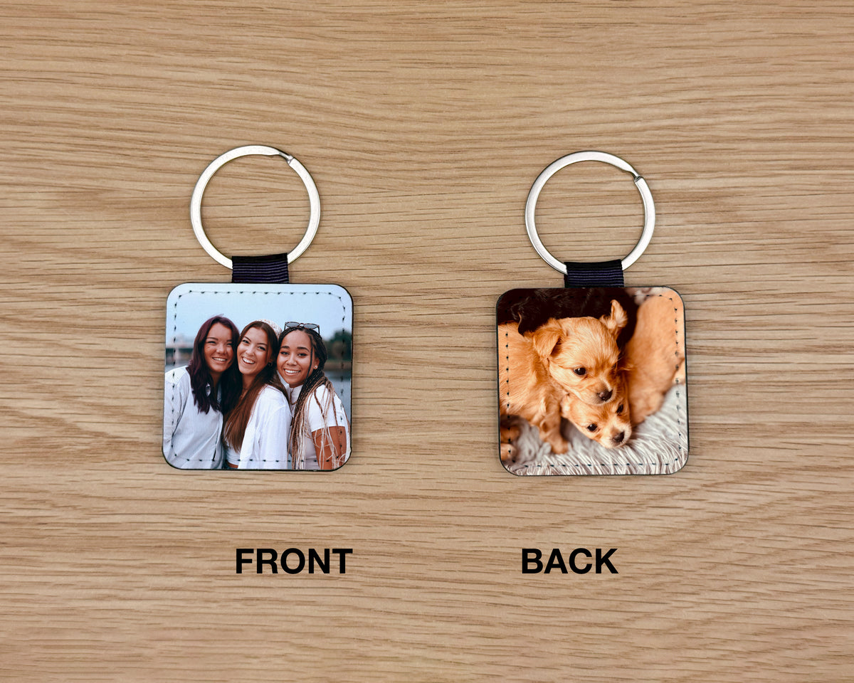 Two square leather keychains shown on a wood surface, labeled FRONT and BACK. The front keychain shows a photo of three women, and the back keychain shows a close-up photo of two dogs.