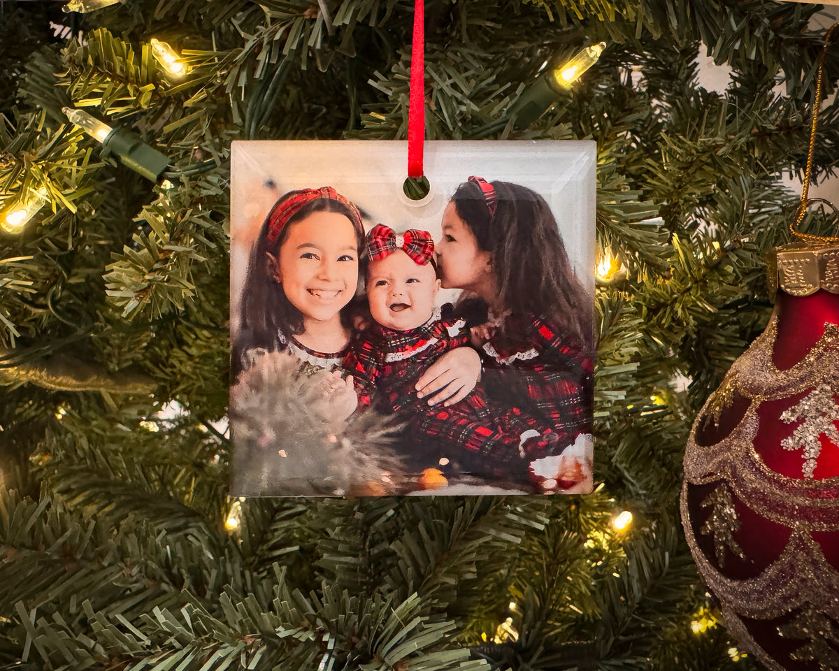 Personalized square glass photo ornament with beveled edges featuring a family portrait, hanging on a Christmas tree.