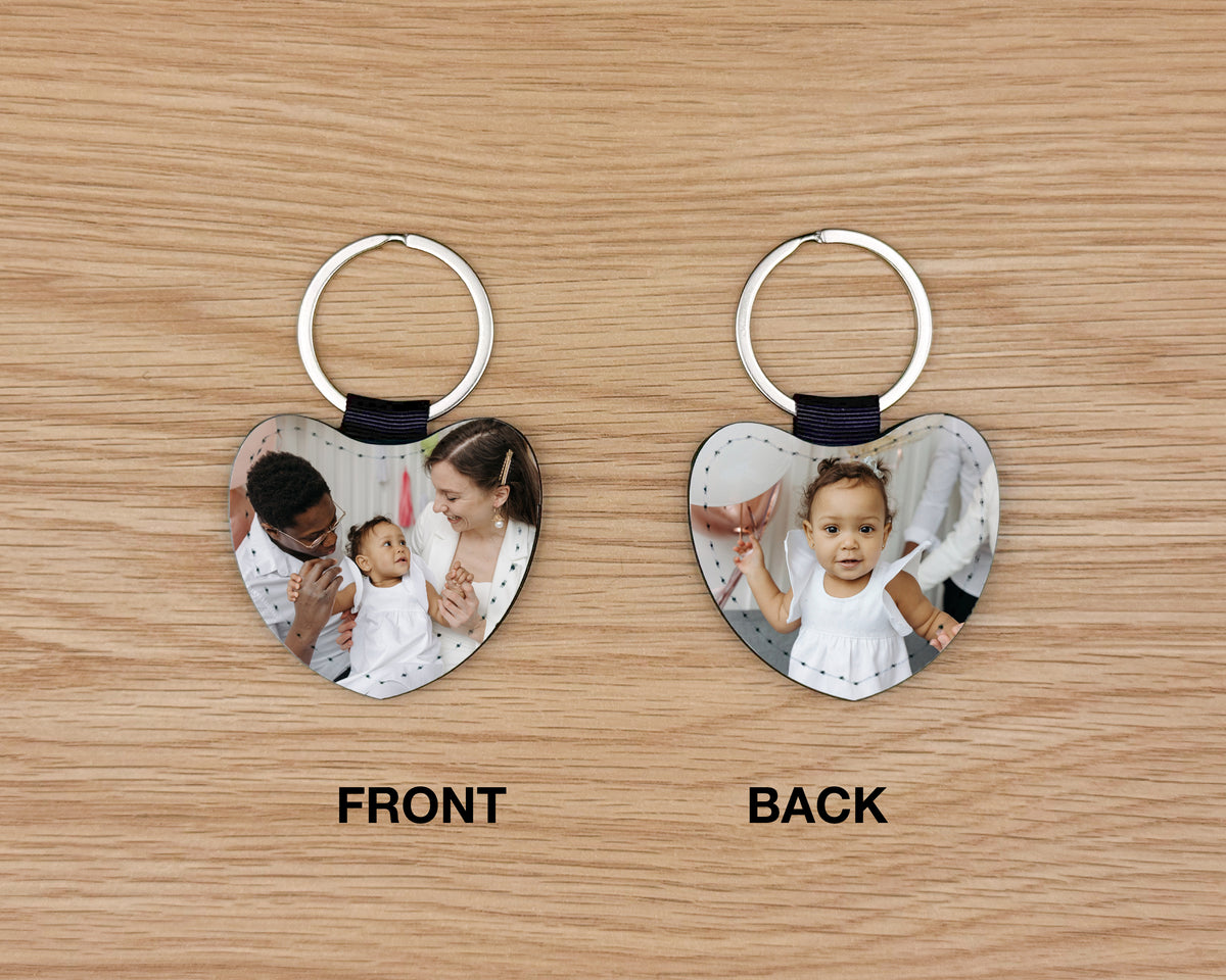 Two heart-shaped custom photo keychains shown side by side on a light wood background, labeled FRONT and BACK. Each keychain has a silver metal split ring, a black connector, and a heart-shaped printed photo panel.