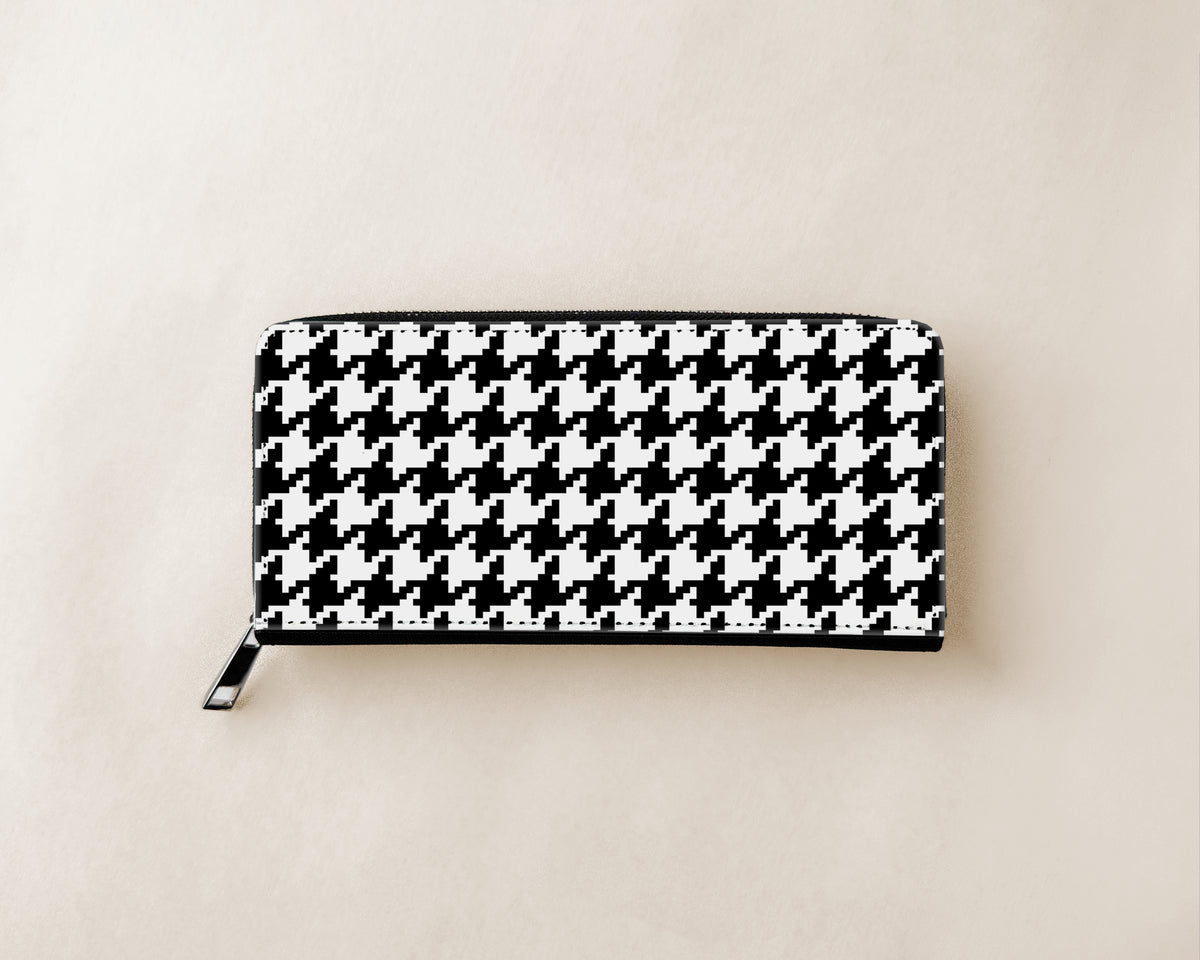 A black and white houndstooth patterned zip-around wallet with a silver zipper pull, shown flat on a light beige background.