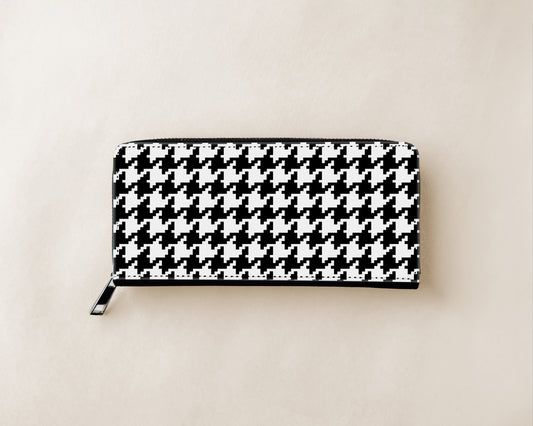A black and white houndstooth patterned zip-around wallet with a silver zipper pull, shown flat on a light beige background.
