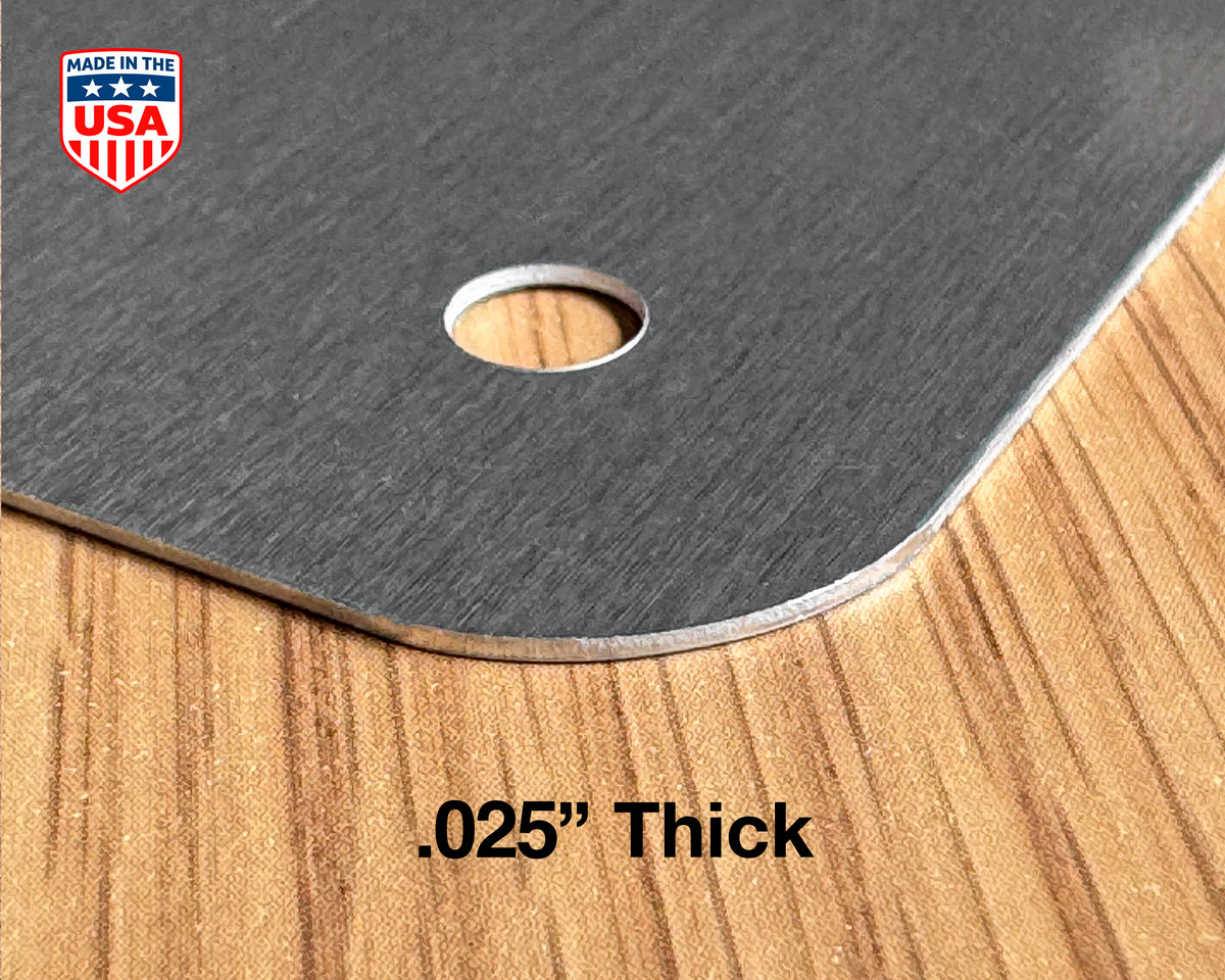 Close-up of a dark gray brushed metal sheet with rounded corners and a circular hole, placed on a wood-grain surface. Text reads '.