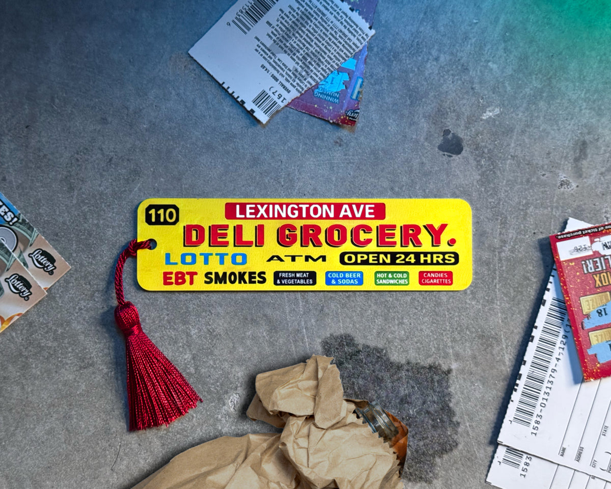 Urban-inspired aluminum bookmark displayed on textured concrete with warm light glow effect. Surrounded by subtle street details for a bold city aesthetic. Slim metal bookmark with tassel, perfect gift for readers, book lovers, students, and anyone who loves unique modern book accessories.