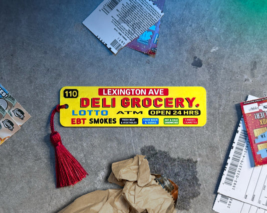 Urban-inspired aluminum bookmark displayed on textured concrete with warm light glow effect. Surrounded by subtle street details for a bold city aesthetic. Slim metal bookmark with tassel, perfect gift for readers, book lovers, students, and anyone who loves unique modern book accessories.