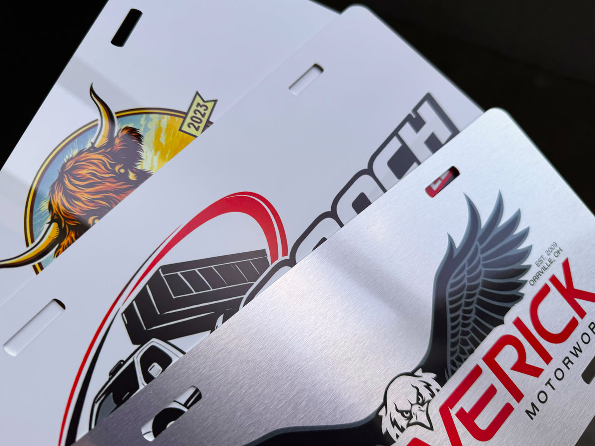 Three custom metal license plates with a brushed silver finish, featuring various graphic designs including a bison, an eagle, and bold text.