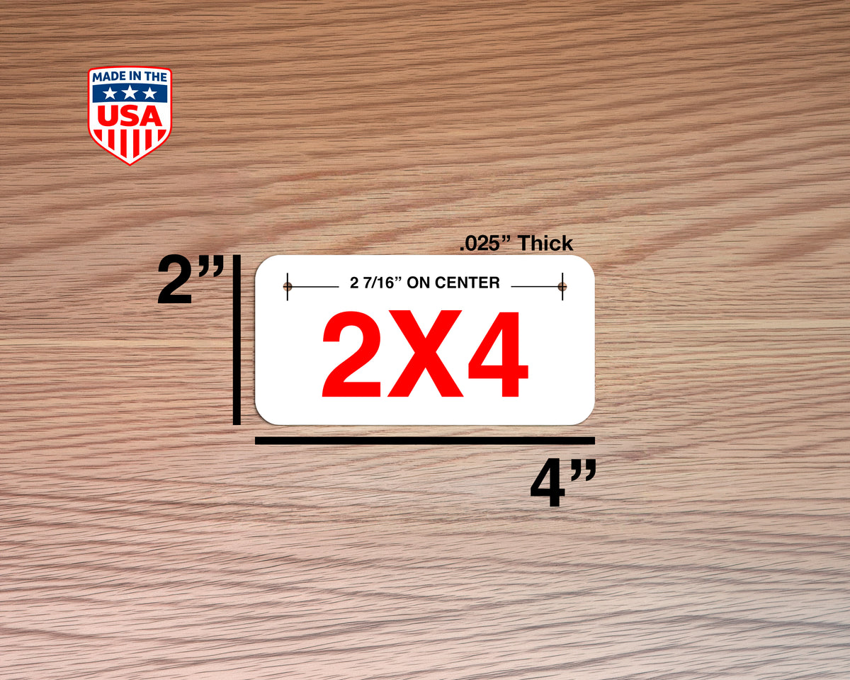 A white rectangular license plate labeled '2X4' in red text, shown with dimension annotations indicating 2 by 4 inches and a thickness of .025 inches, on a wood-grain background.