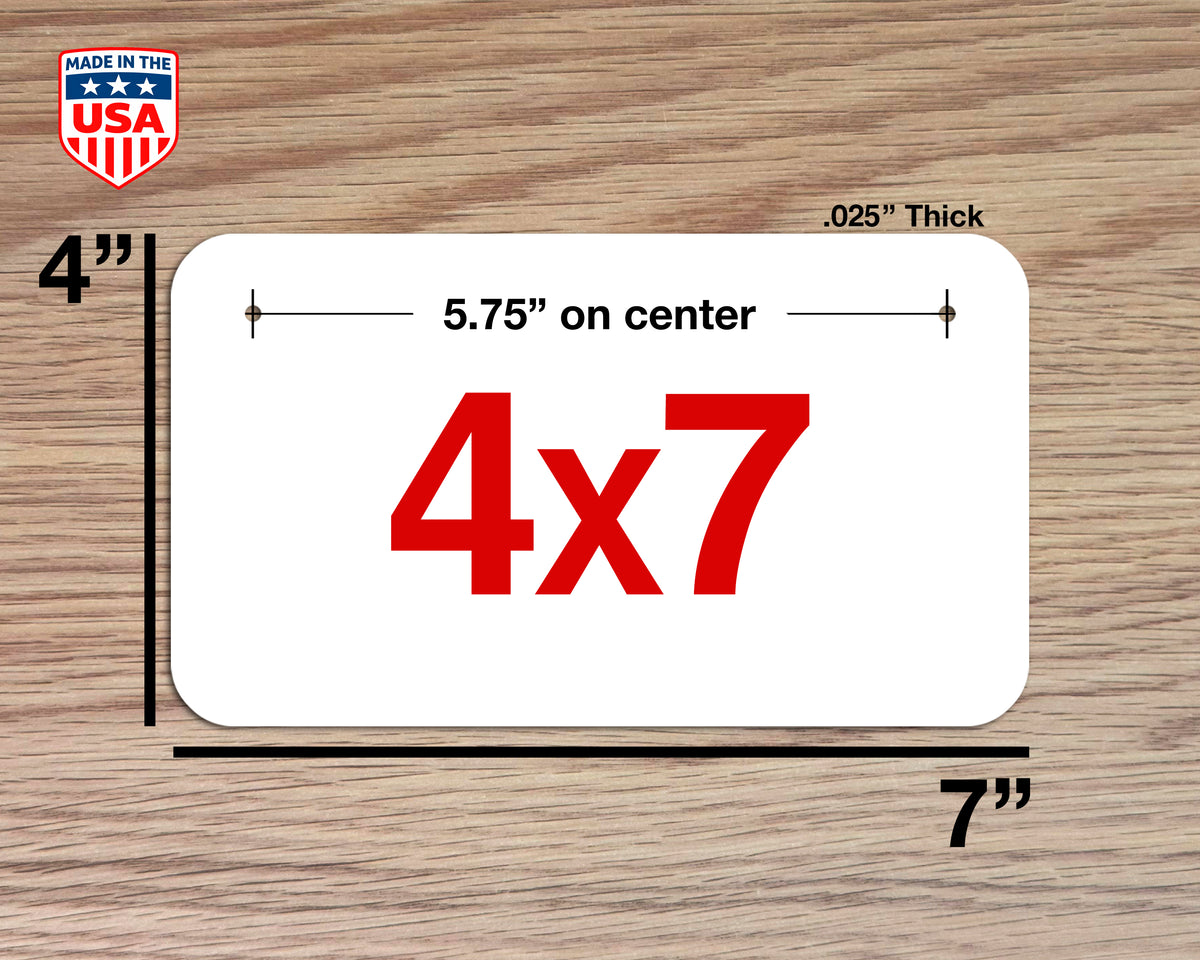A white rectangular plaque or sign with rounded corners, shown on a wood surface with dimension labels. The sign has large red '4x7' text in the center and black measurement lines indicating 5.