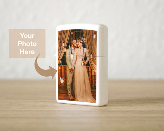 A white rectangular lighter or case standing on a light wood surface against a soft beige wall. The front has a printed custom photo of a couple embracing, with a tan placeholder box and arrow reading 'Your Photo Here' indicating customization.