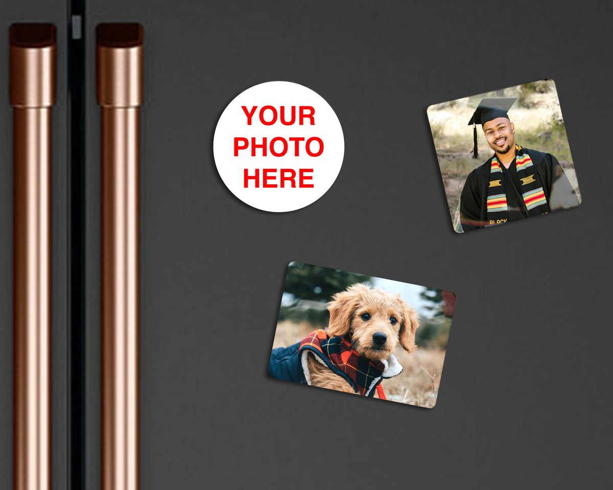 Custom photo magnet set on a dark gray refrigerator, featuring two sample photo magnets, a white circular placeholder magnet with red text reading 'YOUR PHOTO HERE', and two tall rose gold refrigerator door handles on the left.