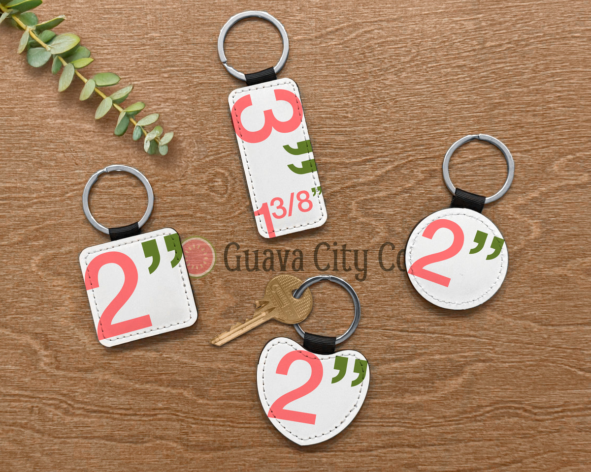 Four white leather keychains with silver metal rings are arranged on a brown wooden surface. The keychains feature sizes of each shape