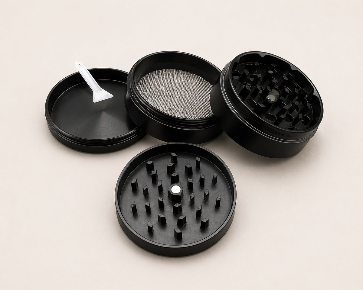 Open black four-piece herb grinder showing the magnetic lid, grinding teeth, fine-mesh screen, collection chamber and scraper tool.