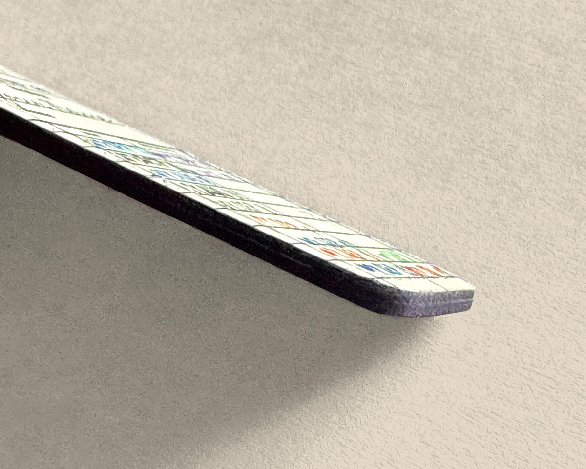 A close-up of a rectangular keychain with a library card due date design on one side and a dark edge, resting diagonally on a textured light gray surface.