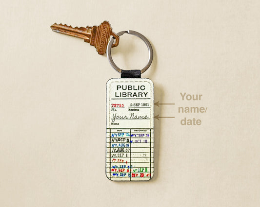 A novelty keychain shaped like a vintage library card attached to a silver key ring. The card has printed fields and handwritten-style entries in multiple colors, with a small label pointing to the name field that reads 'Your name/date'.