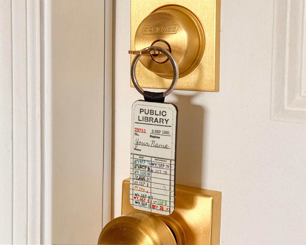 A brass doorknob lock with a key ring holding a white Public Library card, mounted on a white door.