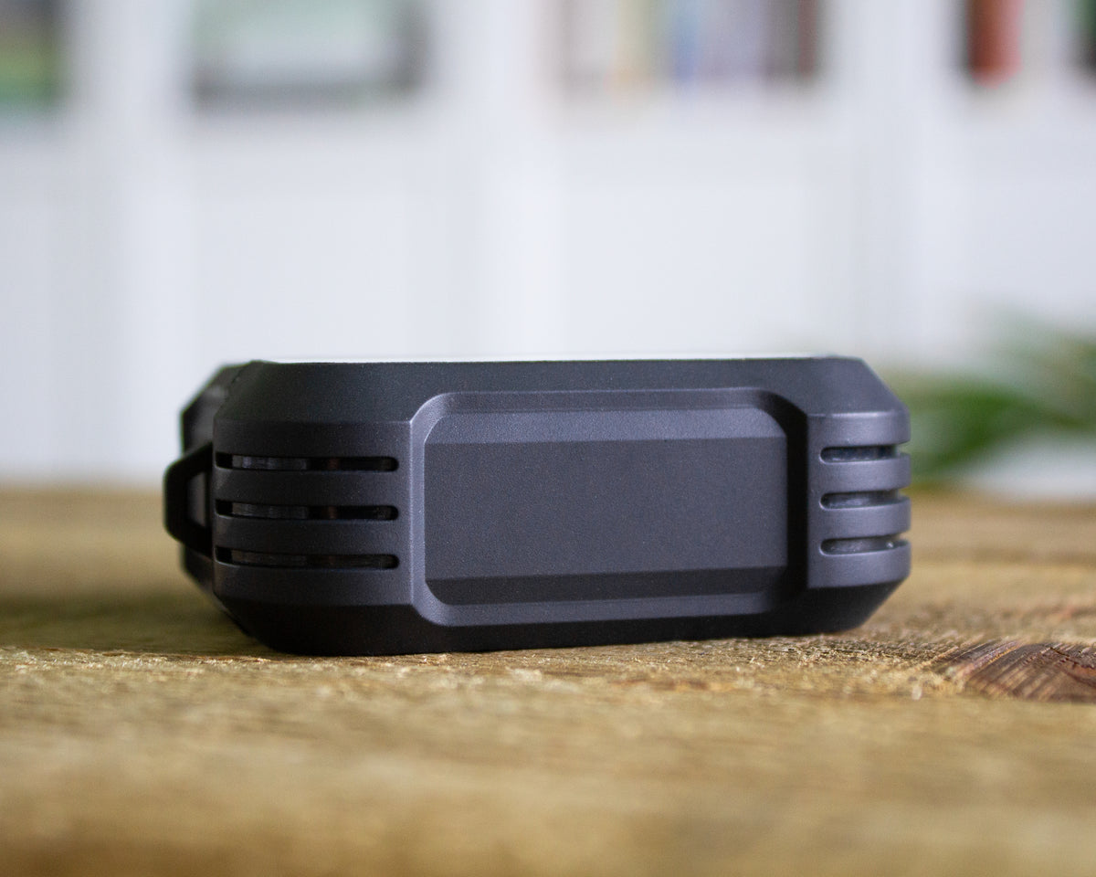 A black rubber AirPods Pro 1st 2nd or 3rd Gen case resting on a wooden surface with a blurred indoor background.