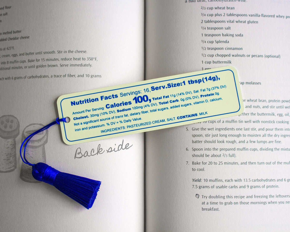 A yellow salted butter metal bookmark recipe card with a blue nutrition facts label, placed on top of an open cookbook page.