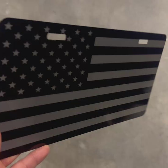 Video of a black and silver brushed metal USA flag lnovelty license plate with a 2 hole mount.